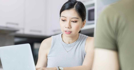 A woman looking at a laptop while reviewing something with another person who is not fully seen