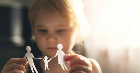 A young girl holding paper figures of two larger people and one smaller person in the middle