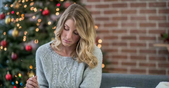 A sad woman looking down at something while a Christmas tree is in the background