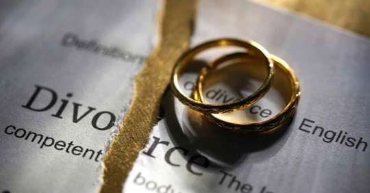 Two wedding rings resting on a ripped piece of paper that reads "Divorce"