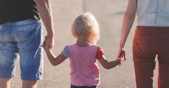 A mother and father walking with their daughter holding hands.